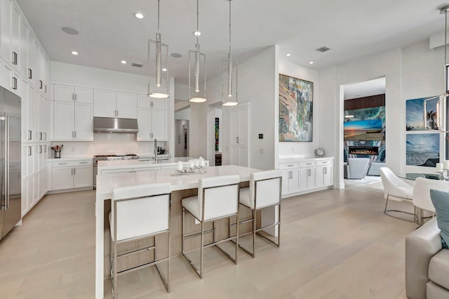 kitchen featuring decorative backsplash, a center island with sink, white cabinetry, stainless steel range with gas cooktop, and hanging light fixtures