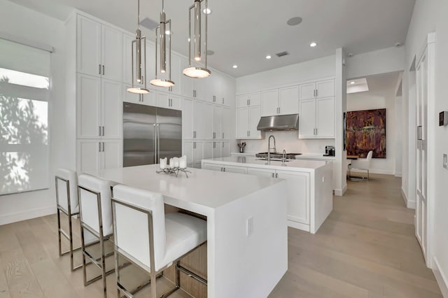 kitchen featuring appliances with stainless steel finishes, pendant lighting, a center island with sink, light hardwood / wood-style flooring, and white cabinets