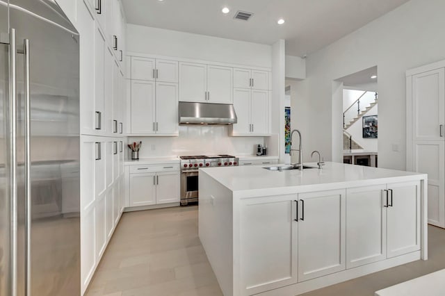 kitchen featuring backsplash, stainless steel appliances, sink, a center island with sink, and white cabinets