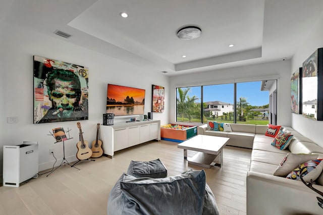 living room with a tray ceiling and light hardwood / wood-style flooring