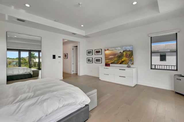 bedroom with a tray ceiling and light wood-type flooring