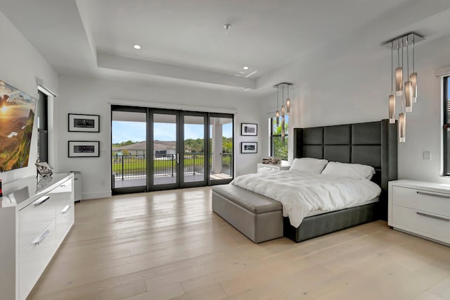 bedroom featuring a raised ceiling, light hardwood / wood-style floors, access to exterior, and french doors