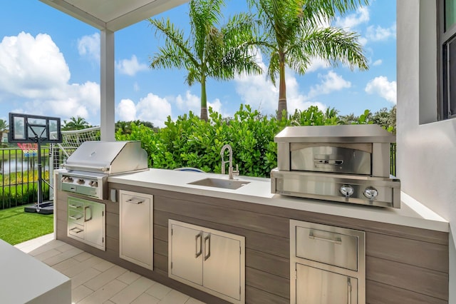 view of patio with sink, a grill, a water view, and exterior kitchen