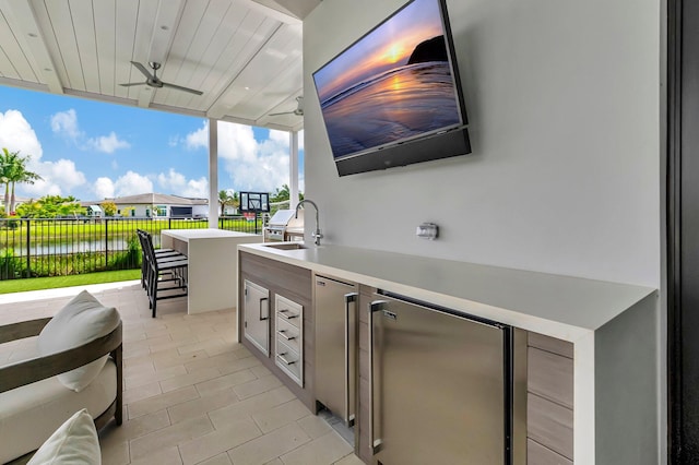 view of patio with exterior kitchen, ceiling fan, a water view, and a wet bar