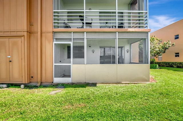 rear view of house with a balcony, a sunroom, and a yard