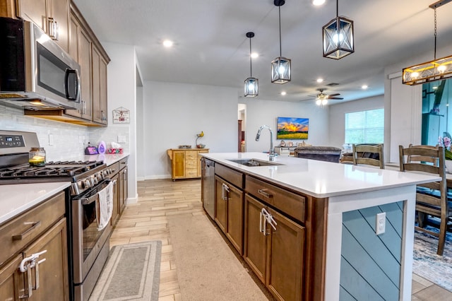 kitchen featuring a kitchen island with sink, sink, light hardwood / wood-style flooring, appliances with stainless steel finishes, and decorative light fixtures