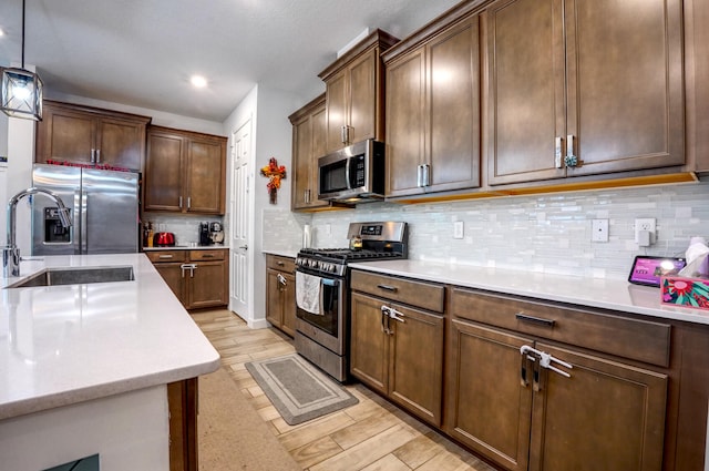 kitchen with pendant lighting, appliances with stainless steel finishes, backsplash, and light hardwood / wood-style floors