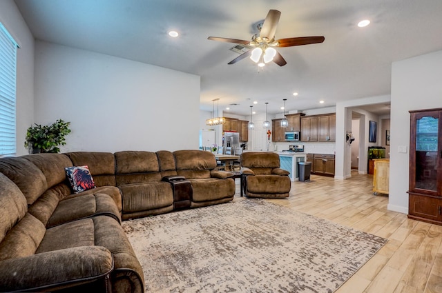 living room with ceiling fan with notable chandelier and light wood-type flooring