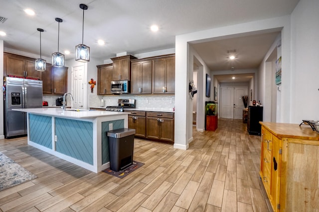 kitchen featuring appliances with stainless steel finishes, decorative light fixtures, light hardwood / wood-style floors, and an island with sink