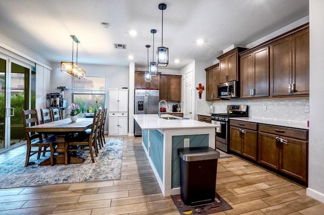 kitchen featuring decorative light fixtures, an island with sink, stainless steel appliances, and a wealth of natural light