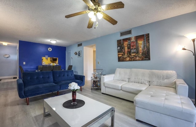 living room featuring ceiling fan, a textured ceiling, and light wood-type flooring