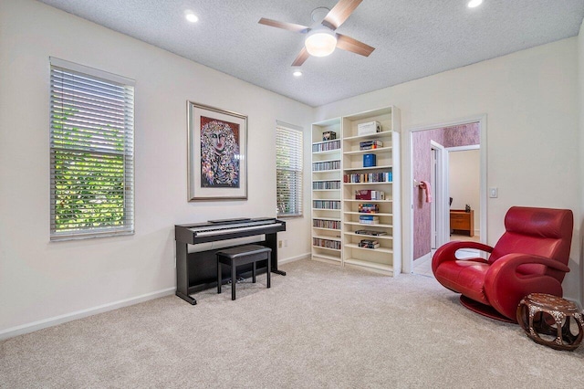 living area with ceiling fan, a textured ceiling, and light colored carpet