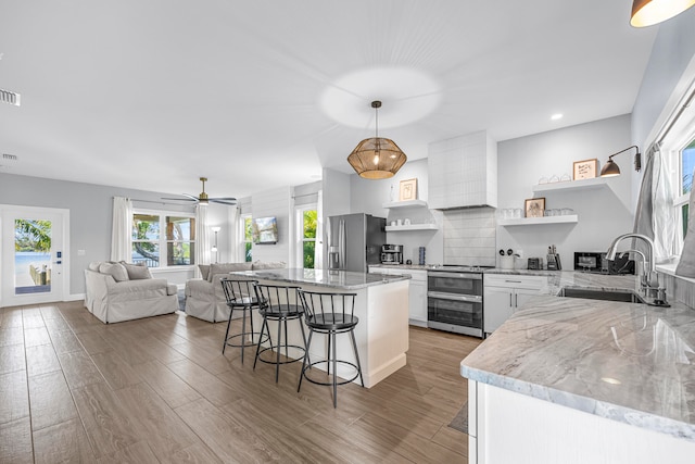 kitchen featuring white cabinetry, a breakfast bar area, pendant lighting, stainless steel appliances, and wood-type flooring