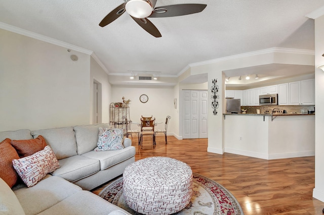 living room with ceiling fan, a textured ceiling, light wood-type flooring, and ornamental molding