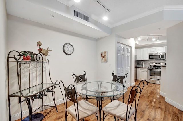 dining space featuring ornamental molding, light hardwood / wood-style floors, and rail lighting