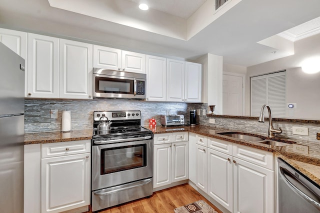 kitchen featuring white cabinetry, tasteful backsplash, stainless steel appliances, dark stone counters, and sink