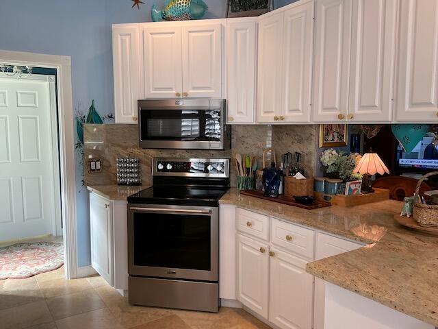 kitchen featuring light stone counters, light tile patterned flooring, stainless steel appliances, backsplash, and white cabinets