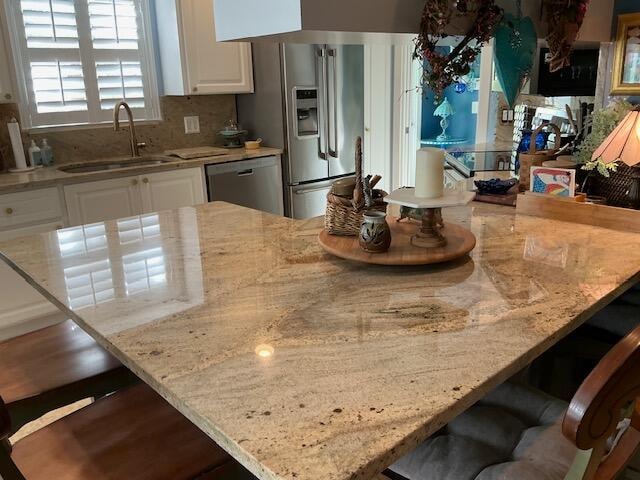 kitchen with a kitchen bar, stainless steel appliances, light stone counters, white cabinets, and sink