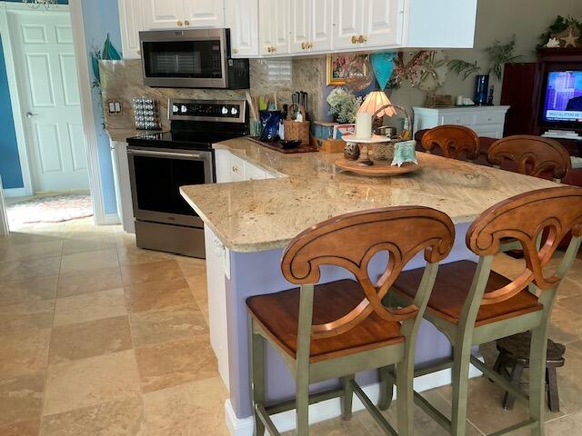 kitchen with light stone counters, stainless steel appliances, backsplash, white cabinets, and kitchen peninsula