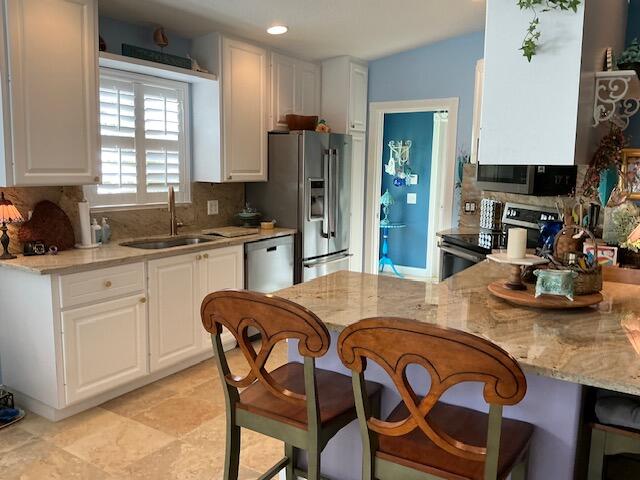 kitchen with stainless steel appliances, backsplash, sink, white cabinets, and kitchen peninsula