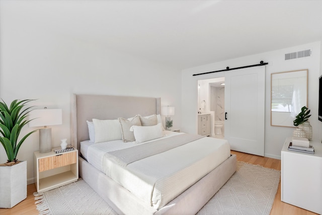 bedroom with a barn door, ensuite bath, and light hardwood / wood-style flooring