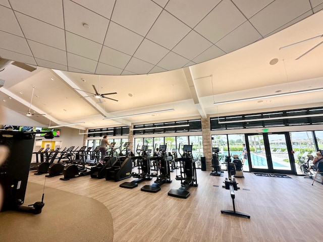 exercise room with ceiling fan, french doors, hardwood / wood-style floors, and a towering ceiling