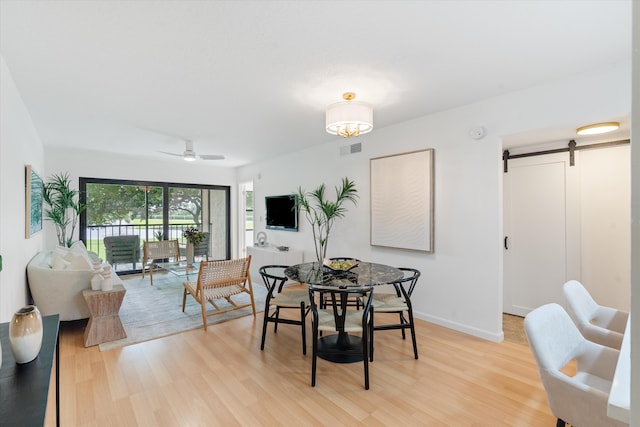 dining room featuring light hardwood / wood-style floors, ceiling fan, and a barn door