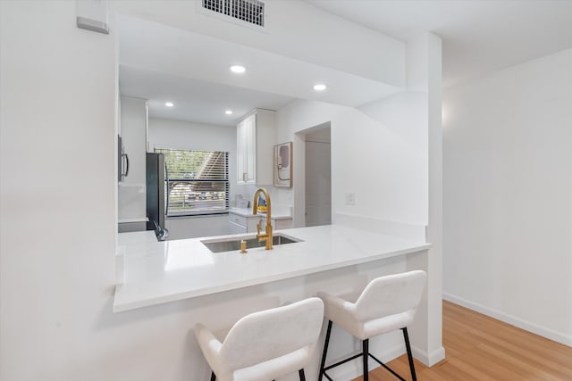 kitchen with kitchen peninsula, white cabinetry, stainless steel appliances, a breakfast bar, and light hardwood / wood-style floors