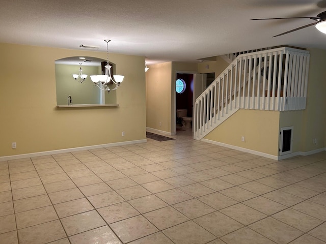 tiled empty room with a textured ceiling and ceiling fan with notable chandelier