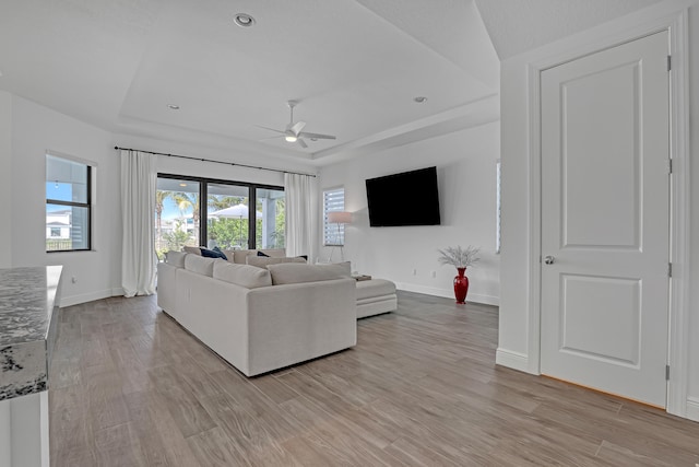 living room with ceiling fan, light hardwood / wood-style floors, and a raised ceiling