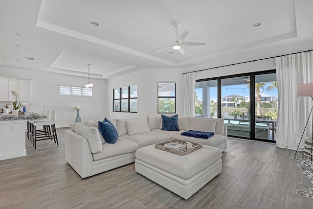 living room featuring ceiling fan with notable chandelier and a raised ceiling