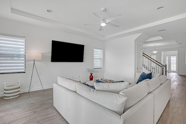 living room featuring ceiling fan, light wood-type flooring, and a tray ceiling