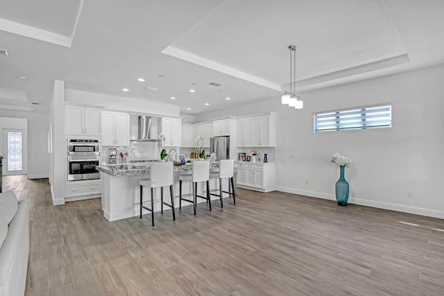 kitchen featuring appliances with stainless steel finishes, white cabinetry, wall chimney exhaust hood, and a tray ceiling