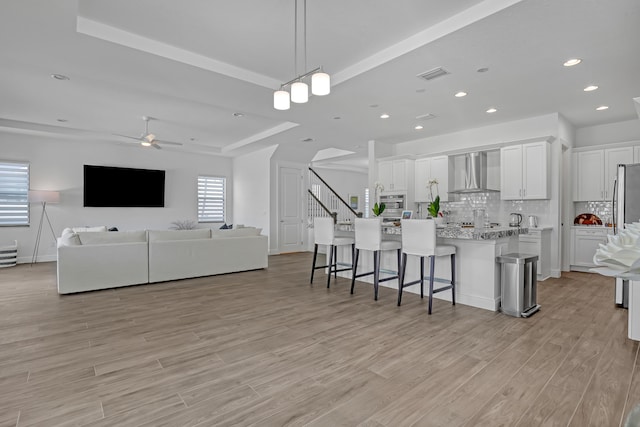 kitchen featuring decorative light fixtures, white cabinetry, a kitchen breakfast bar, an island with sink, and wall chimney exhaust hood