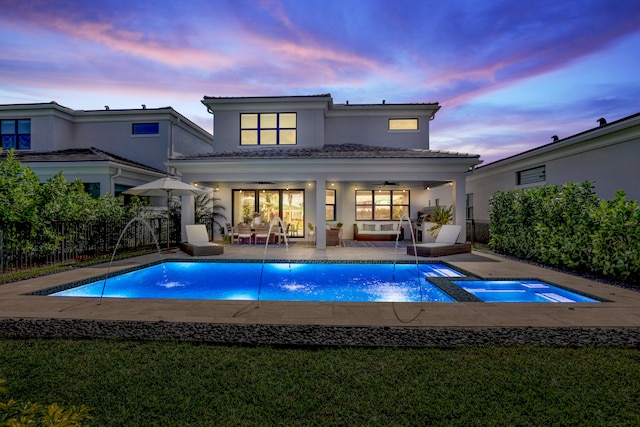 pool at dusk with ceiling fan, pool water feature, an in ground hot tub, and a patio