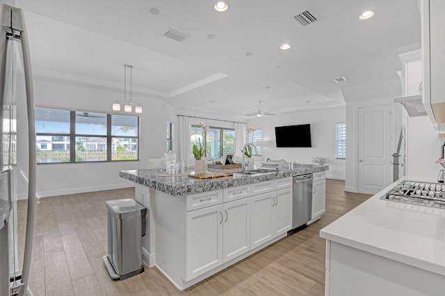 kitchen featuring ceiling fan, a raised ceiling, sink, an island with sink, and white cabinets