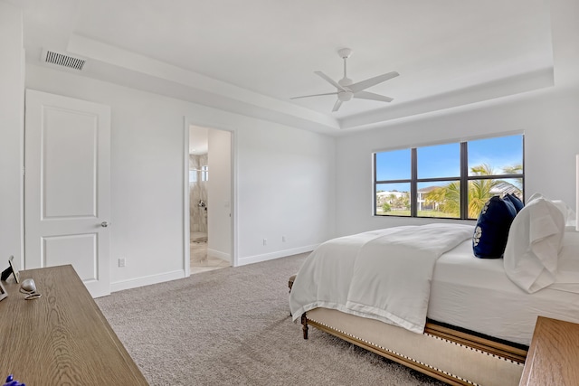 bedroom with ceiling fan, carpet, a tray ceiling, and ensuite bath