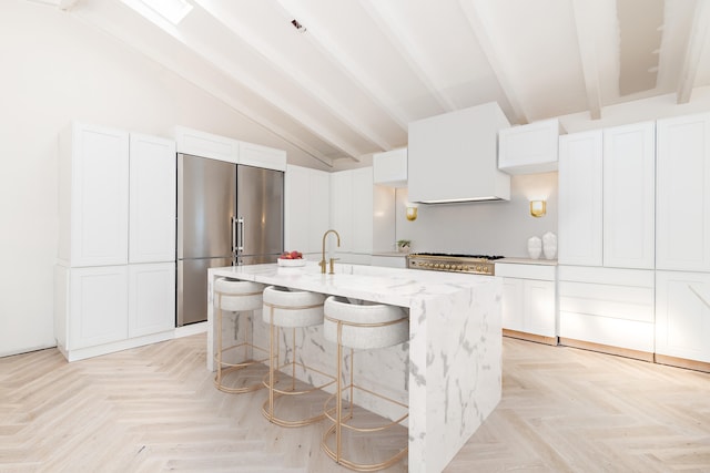 kitchen with appliances with stainless steel finishes, vaulted ceiling with beams, white cabinetry, and a kitchen island with sink