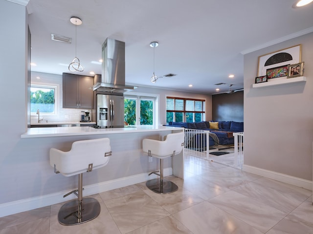 kitchen with island exhaust hood, stainless steel refrigerator with ice dispenser, light countertops, a kitchen bar, and tasteful backsplash