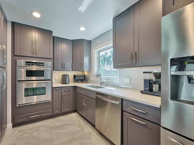 kitchen featuring stainless steel appliances, a sink, light countertops, gray cabinetry, and recessed lighting
