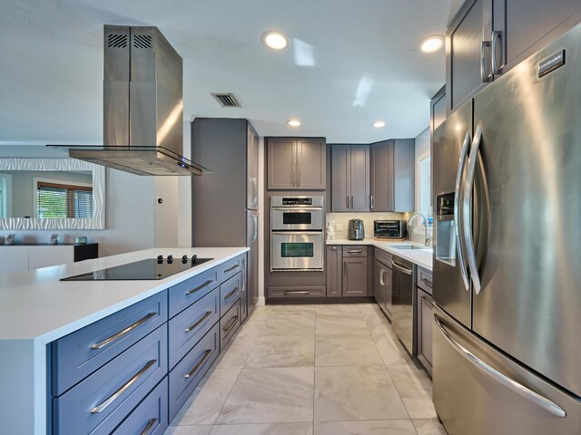 kitchen featuring appliances with stainless steel finishes, island range hood, light marble finish flooring, light countertops, and a sink