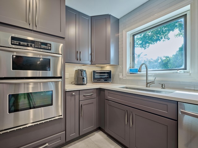 kitchen featuring stainless steel appliances, gray cabinets, a sink, and light countertops