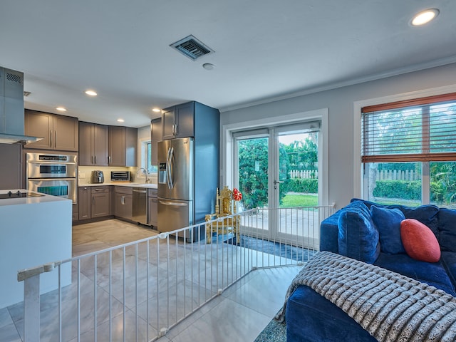 interior space featuring stainless steel appliances, sink, ornamental molding, light tile patterned floors, and french doors