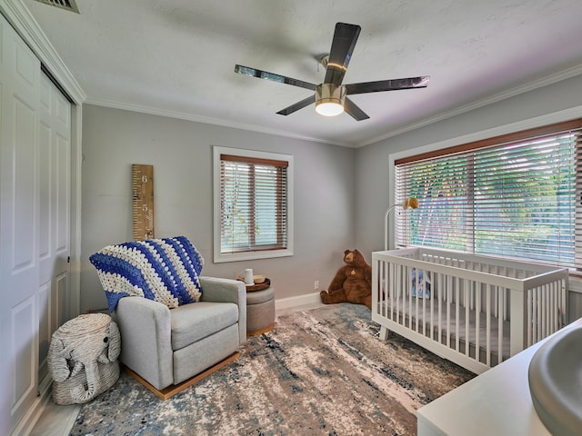 bedroom with a closet, crown molding, baseboards, a crib, and wood finished floors