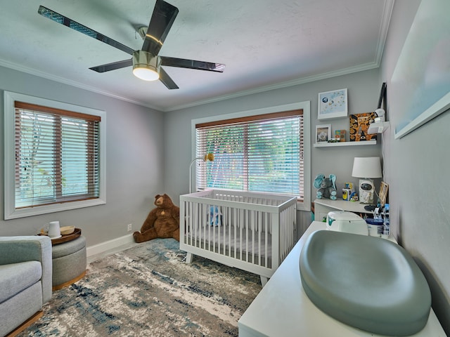 bedroom featuring a nursery area, ornamental molding, a ceiling fan, and baseboards