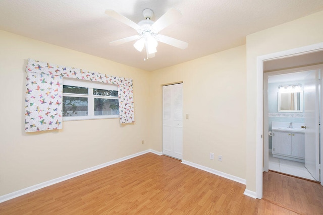 unfurnished bedroom with ceiling fan, sink, light wood-type flooring, and a closet