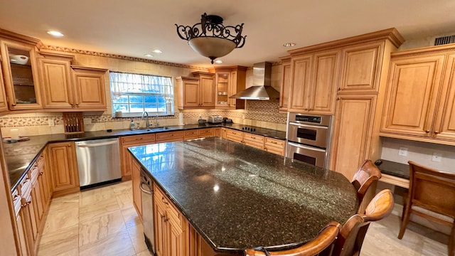 kitchen with appliances with stainless steel finishes, a kitchen breakfast bar, sink, wall chimney range hood, and dark stone countertops