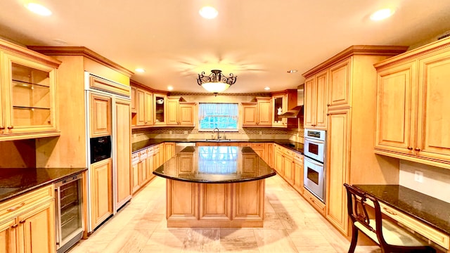 kitchen with wall chimney range hood, sink, light brown cabinetry, a kitchen island, and beverage cooler