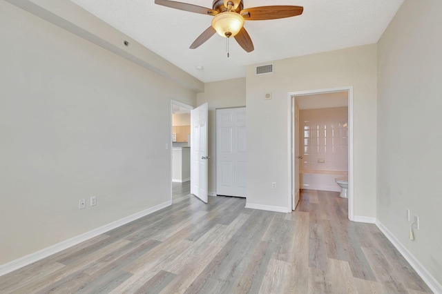 unfurnished bedroom featuring ceiling fan, a textured ceiling, ensuite bath, and light hardwood / wood-style floors