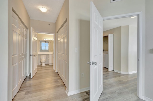 hallway with light hardwood / wood-style floors, a textured ceiling, and independent washer and dryer